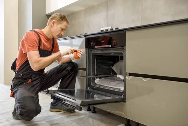 The worker is installing an electric oven in the kitchen furniture.