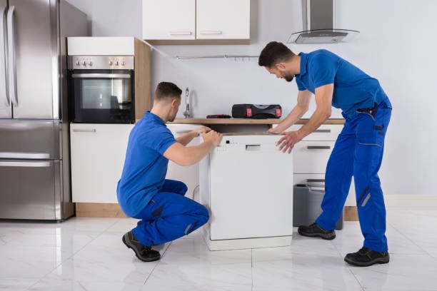 Two Young Male Movers In Uniform Placing Dishwasher In Kitchen